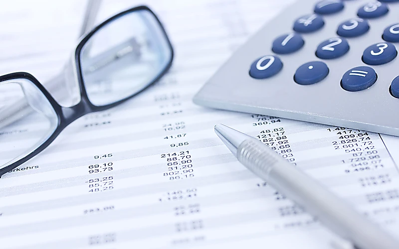 Taschenrechner, Brille und Kugelschreiber liegen auf einer Tabelle mit Zahlen und Finanzdaten.